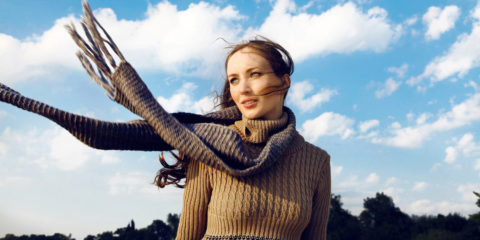 Frau mit Schal und Pullover im Herbst vor blauem Himmel