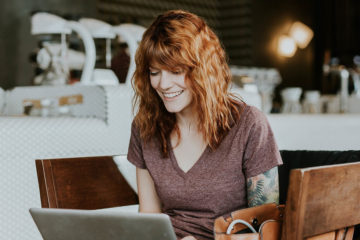 Junge brünette Frau mit Tattoos sitzt im Café am Laptop beim Online-Shopping