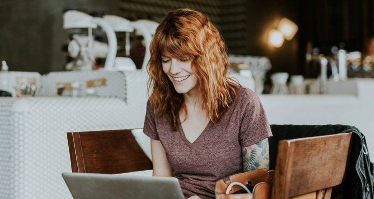 Junge brünette Frau mit Tattoos sitzt im Café am Laptop beim Online-Shopping