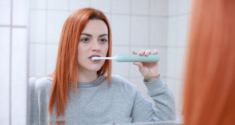 Rothaariges Mädchen beim Zähneputzen mit elektrischer Zahnbürste